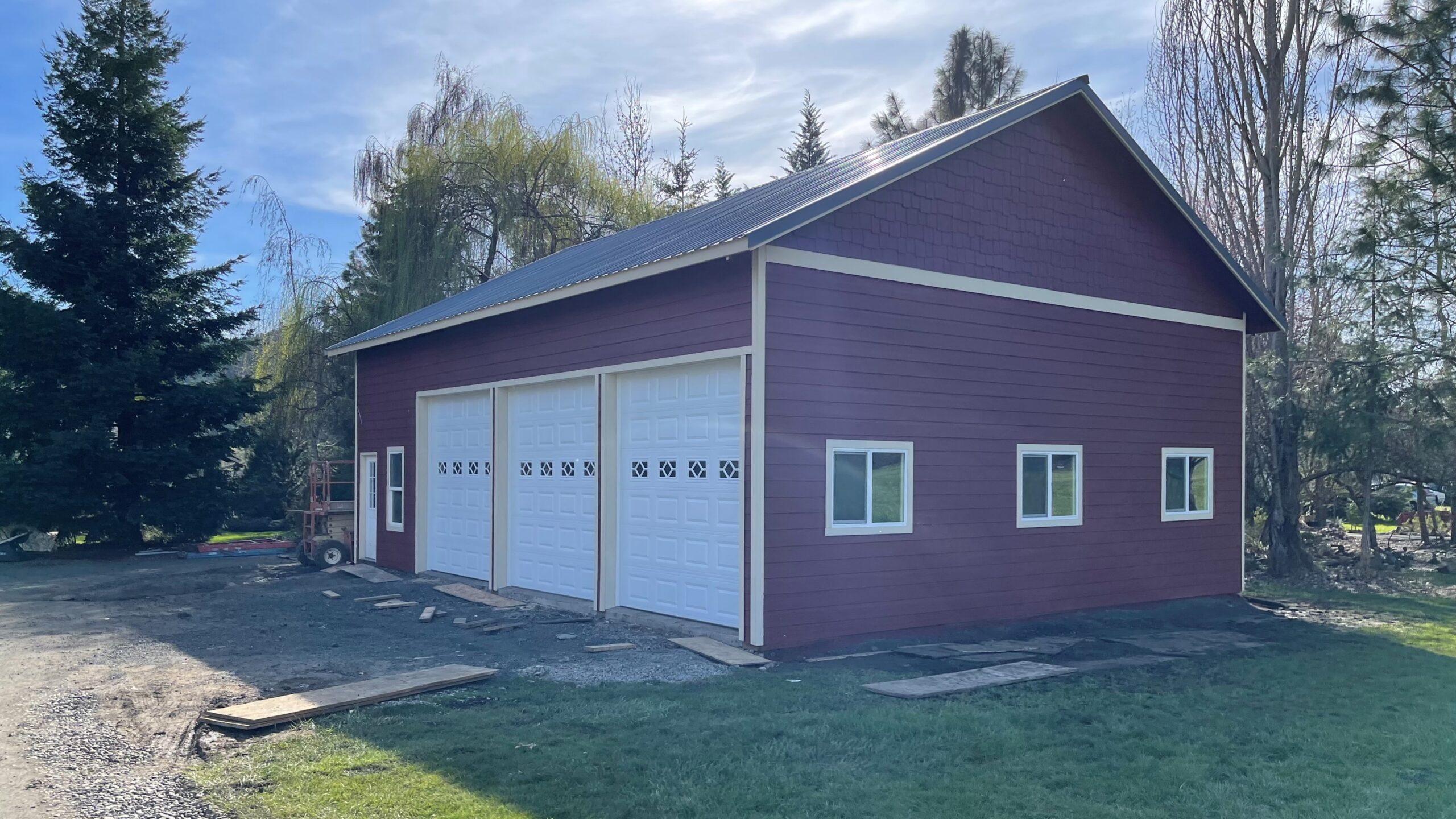 Maroon post frame shop with three white garage doors built by JTW Construction in Douglas County Oregon