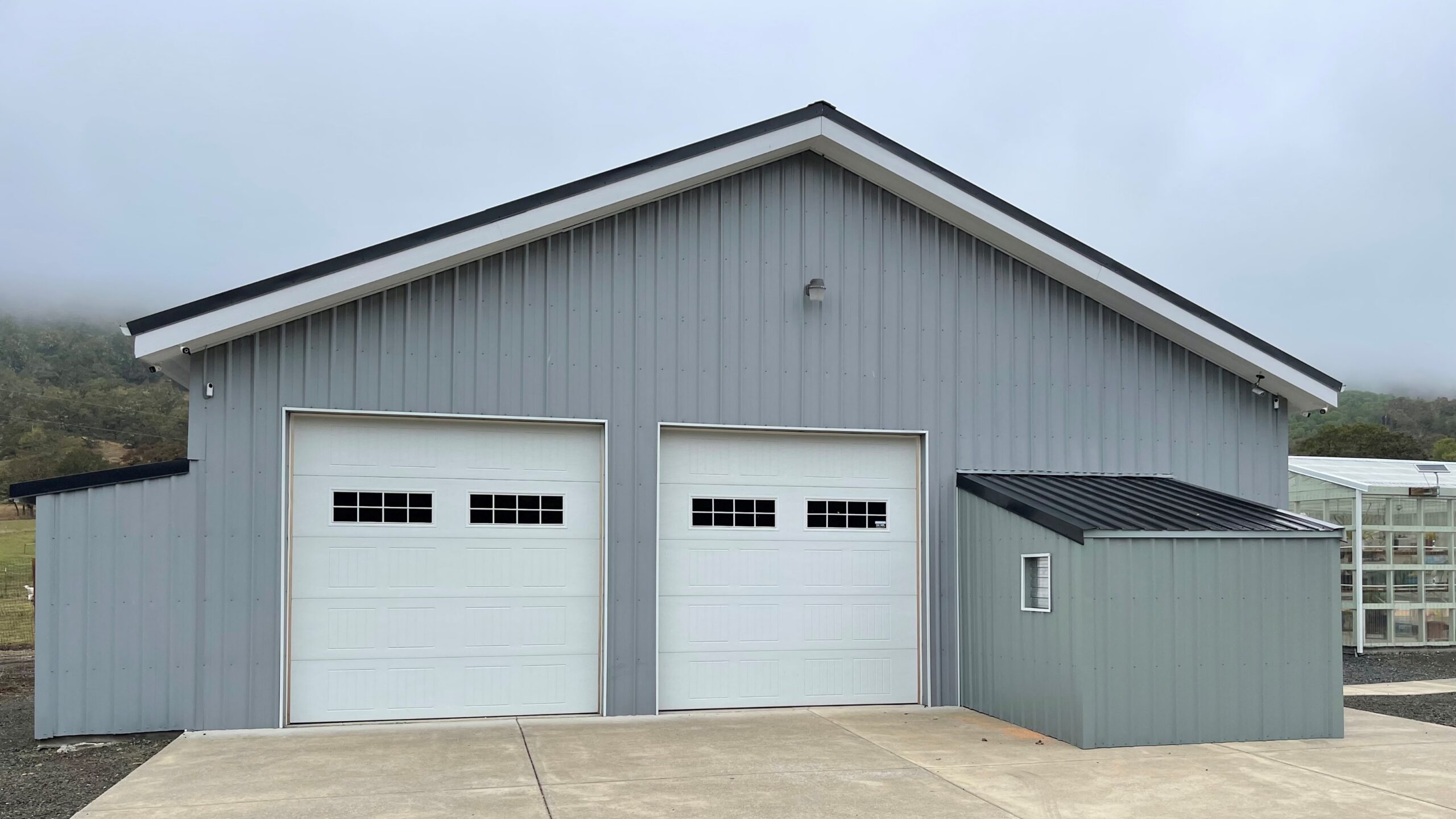 Grey post frame shop with two white garage doors